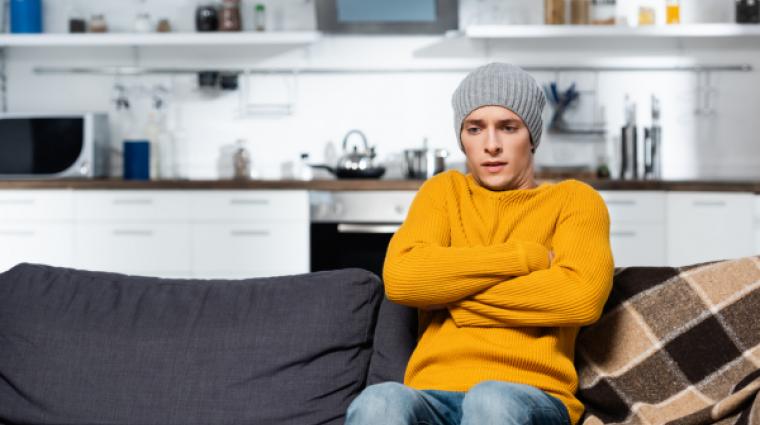 Person sitting on couch with hat, freezing. 