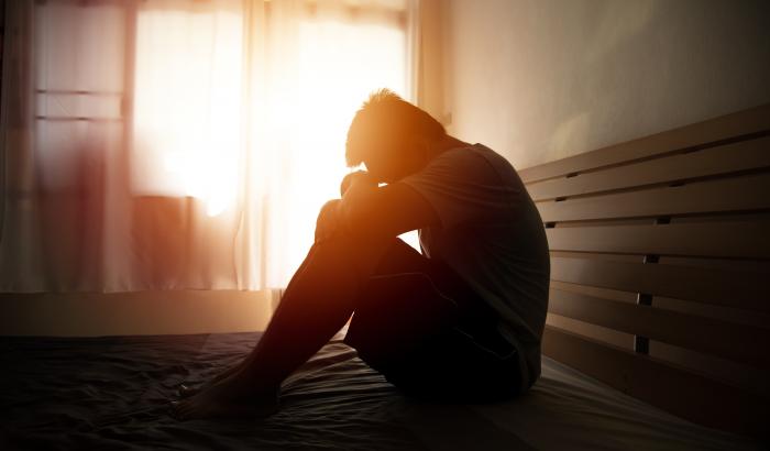 person sitting on bed with head on knees