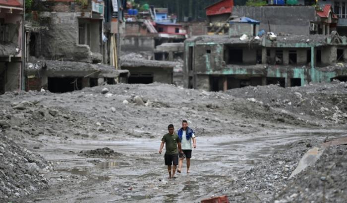 Des habitants traversent, le 30 août 2026, une rue ensevelie sous des tonnes de boue du centre de Trishuli, au Népal, victime d'une crue dévastatrice