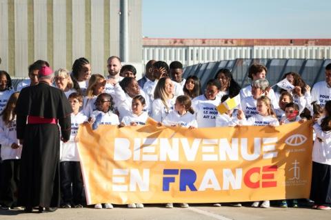 Des personnes se tiennent derrière une banderole sur laquelle on peut lire "Bienvenue en France" alors qu'elles attendent l'arrivée du pape Léon XIV devant l'aéroport d'Orly, dans la banlieue de Paris, le 25 septembre 2026