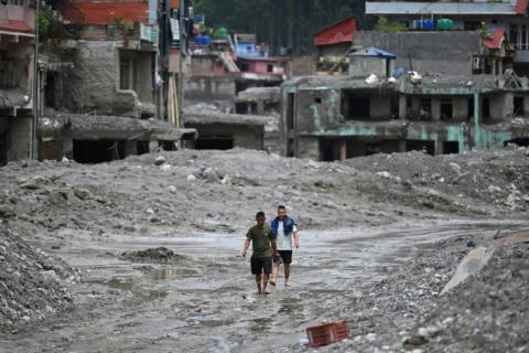 Des habitants traversent, le 30 août 2026, une rue ensevelie sous des tonnes de boue du centre de Trishuli, au Népal, victime d'une crue dévastatrice