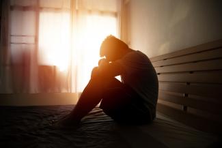 person sitting on bed with head on knees