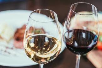 two glasses with wine, one red, one white, with a dinner background