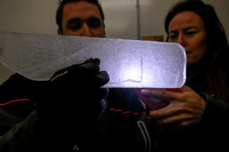 Des scientifiques examinent à la lumière d'un téléphone portable une carotte glaciaire antarctique dans un laboratoire à Bruxelles, le 15 juillet 2025 en Belgique