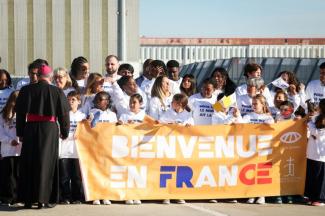 Des personnes se tiennent derrière une banderole sur laquelle on peut lire "Bienvenue en France" alors qu'elles attendent l'arrivée du pape Léon XIV devant l'aéroport d'Orly, dans la banlieue de Paris, le 25 septembre 2026